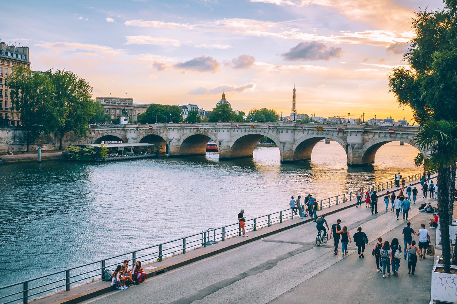 Promeneurs sur les quais de Seine au coucher du soleil, un pont en arrière-plan